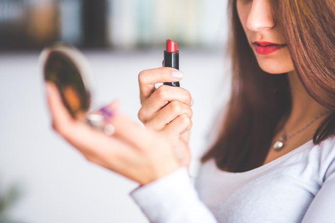 Woman with hand held mirror and lipstick - Why Is My Transgender Wife Better at Being a Girl Than Me - When a partner’s transition changes your perspective about your own gender. – Trans Partners by U.A. Nigro