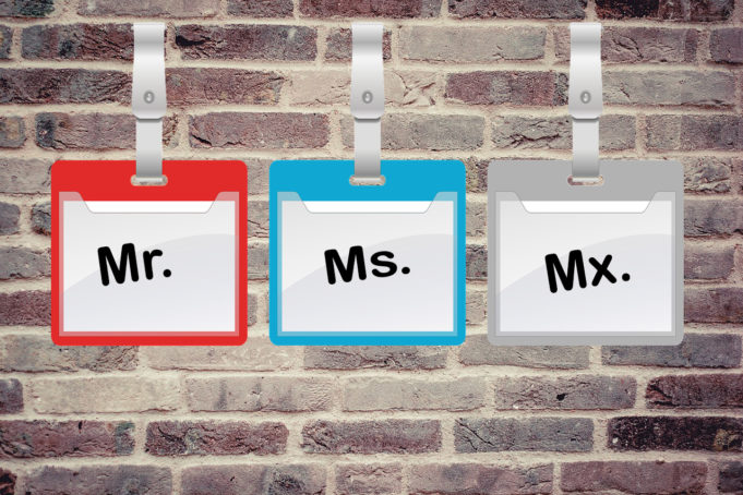 Brick Wall with name tags hanging from it saying Mr., Ms., and MX. - Kameron with a story about the use honorifics such a Mr. and Mrs., and ultimately arriving at the gender-neutral Mx., which is pronounced Mix or Mixter.